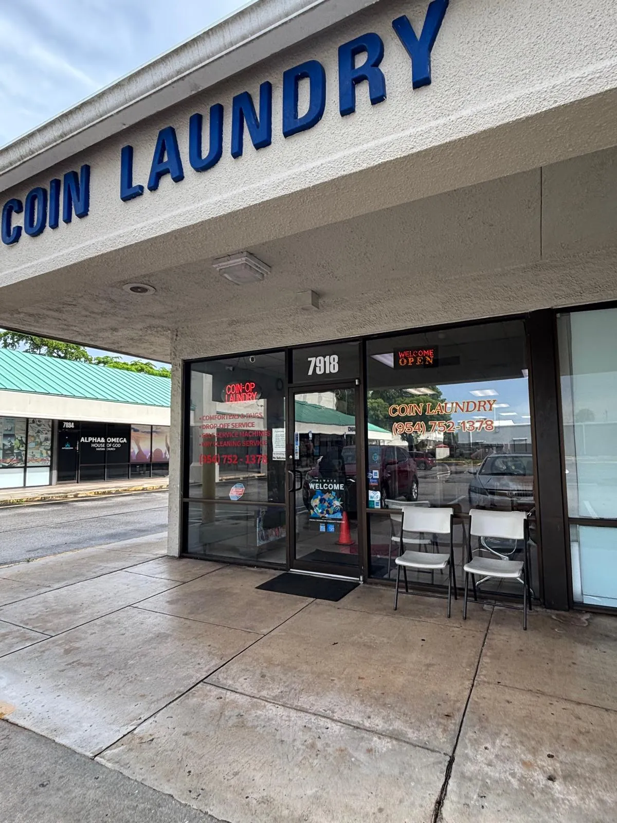 The GJL Coin Laundry storefront at 7918 West Sample Road, with tall blue COIN LAUNDRY letters above the entrance, a lit WELCOME OPEN sign in the window, and red lettering listing comforters and rugs, drop-off service, self-service machines and dry cleaning.